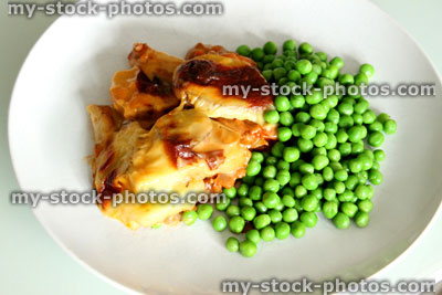 Stock image of portion of moussaka served on white plate with garden peas