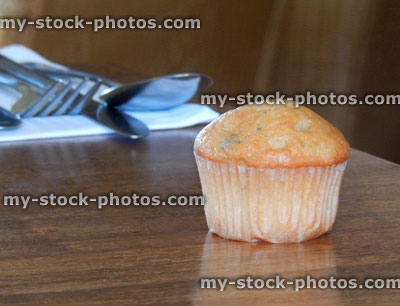 Stock image of freshly baked muffin on wooden table, cutlery, napkin