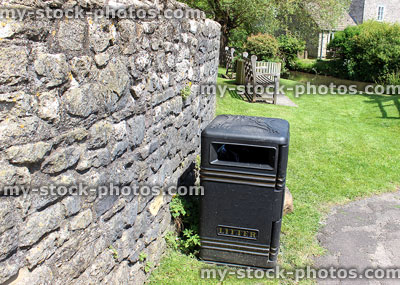 Stock image of litter bin in park, next to cobblestone wall