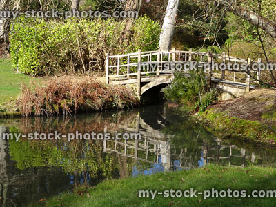 Stock image of arching timber bridge across shallow river, tree reflections