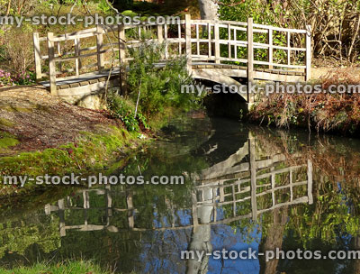 Stock image of wooden arched bridge over small river, water reflections
