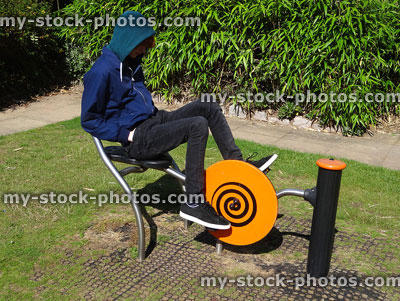 Stock image of teenage boy exercising in public park on exercise bike