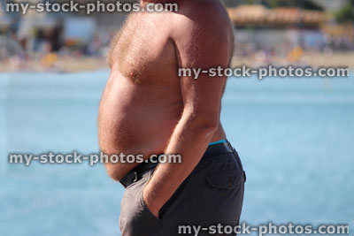 Stock image of overweight topless man at seaside, fat man / beer belly