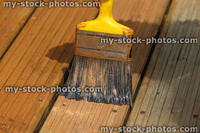 Stock image of paint brush painting wooden decking timber with woodstain