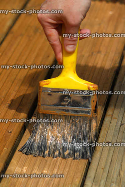 Stock image of yellow paint brush, painting timber decking in garden
