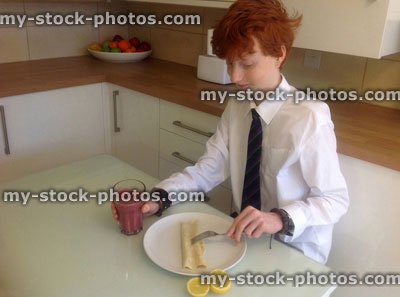 Stock image of boy eating pancakes for breakfast with fruit smoothie