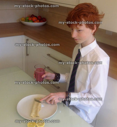 Stock image of boy wearing school uniform eating breakfast, kitchen table
