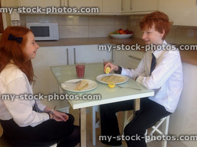 Stock image of children eating pancake breakfast in modern white kitchen