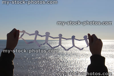 Stock image of people paper chain being held against sea / sky