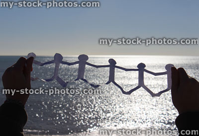 Stock image of paperchain of cut out people in front of sea / sky