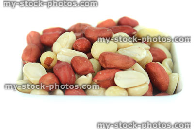 Stock image of mixed red skin peanuts in white dish, white background