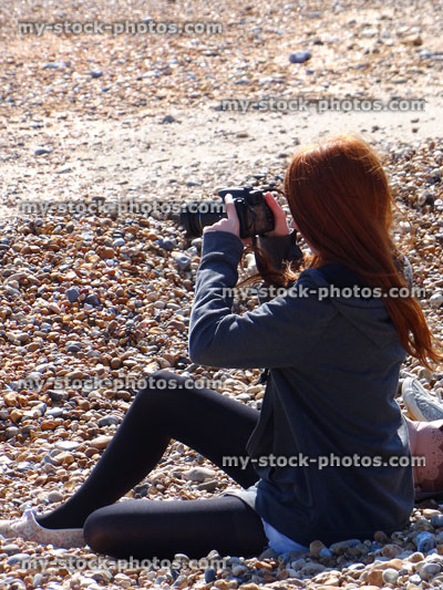 Stock image of girl sitting on beach taking photos with camera