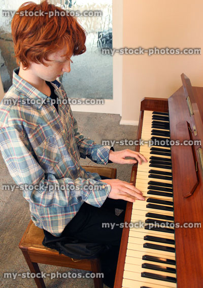 Stock image of teenage boy playing the piano, wooden piano keyboard