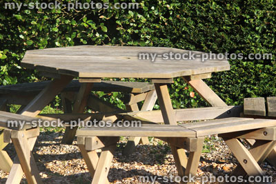 Stock image of round wooden picnic tables, ornamental gravel garden / park, yew hedge
