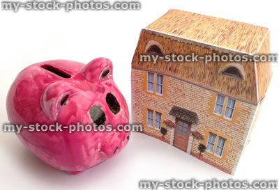 Stock image of pink piggy bank and tiny thatched cottage