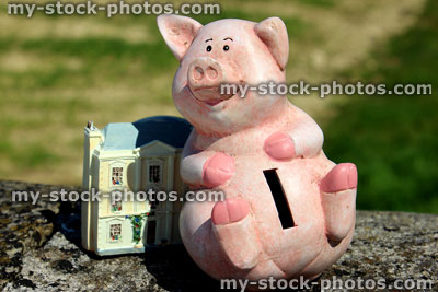 Stock image of cheerful piggy bank and small home / dolls house 