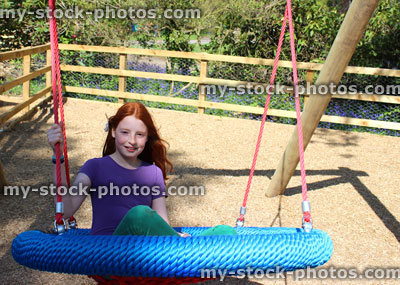 Stock image of young child playing in woodland playground, swinging on cradle swing