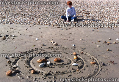 Stock image of boy throwing pebbles at a sand target on the beach