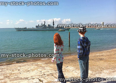 Stock image of two children next to Portsmouth beach, with warship sailing by