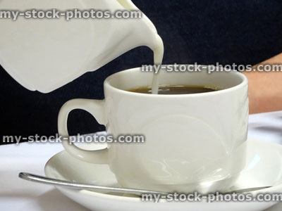 Stock image of pouring milk into cut of black coffee, white china jug