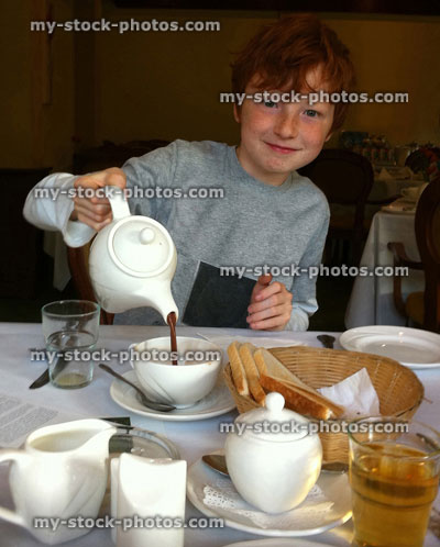 Stock image of red haired boy pouring from teapot at breakfast