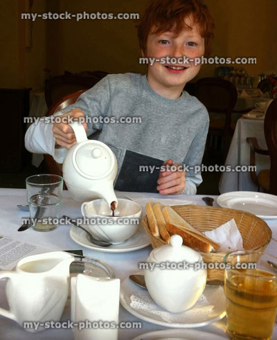 Stock image of red haired boy pouring from teapot at breakfast
