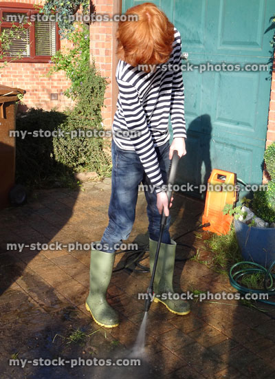 Stock image of boy powerwashing block paved driveway wearing wellie boots