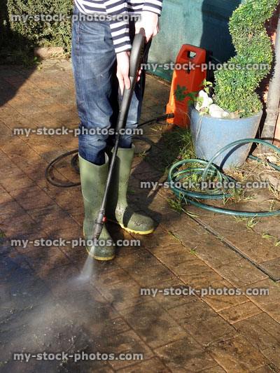 Stock image of boy washing block paved driveway with powerwasher hose pipe