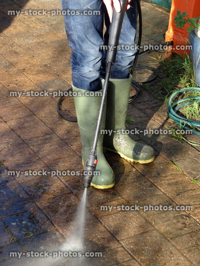 Stock image of boy wearing wellie boots powerwashing / pressure washing block paved drive