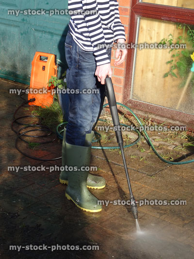 Stock image of boy with wellies powerwashing brick driveway with powerwasher / pressure washer