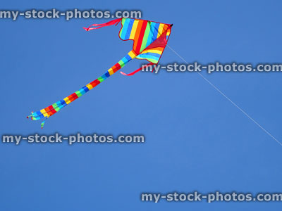 Stock image of kite with rainbow stripes flying against blue sky