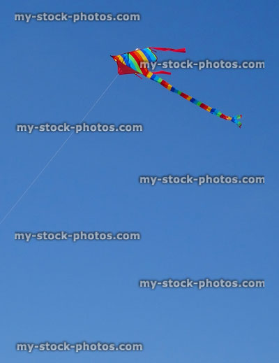 Stock image of kite flying in sky with rainbow stripes / long tail