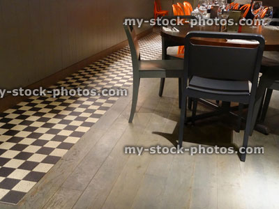 Stock image of wooden restaurant tables chairs / orange seats, wine glasses, cutlery, black and white tiled checkered floor / checkerboard