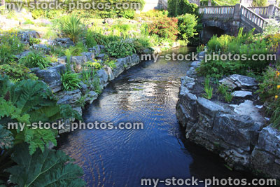 Stock image of stream running through landscaped rockery garden, stone bridge
