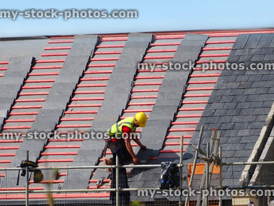 Stock image of roofer placing new slate tiles on roof felt