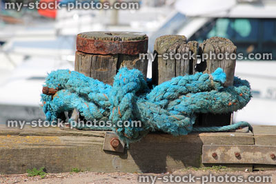 Stock image of blue boat rope tied to mooring post in marina
