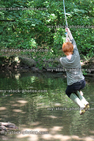 Stock image of boy on rope swing, swinging across river water