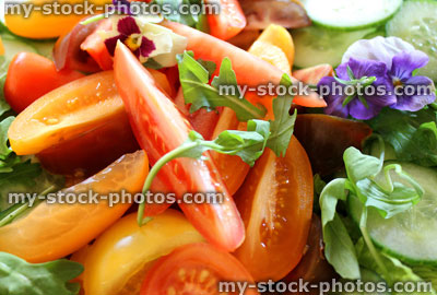 Stock image of green salad with lettuce, cucumber, red and yellow tomatoes, edible flowers