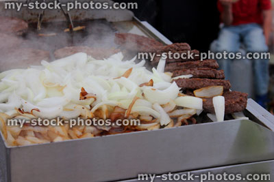 Stock image of beef burgers frying, sliced white onions on griddle / grill pan