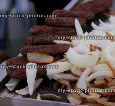 Stock image of beef burgers frying, sliced white onions on griddle / grill pan