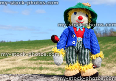 Stock image of friendly knitted scarecrow toy against field background 