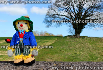 Stock image of friendly knitted scarecrow toy against field background