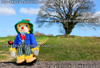 Stock image of friendly knitted scarecrow toy against field background
