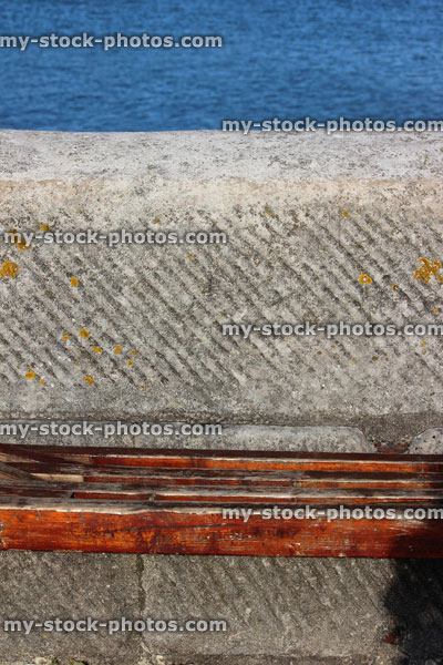 Stock image of simple seaside bench, wooden seat by beach / stone harbour wall
