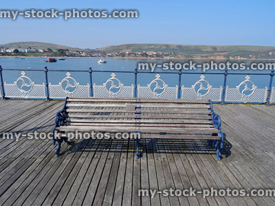 Stock image of seaside pier with ornamental metal bench, balustrading, decking