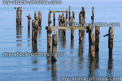 Stock image of seaside wooden pier remains reflecting in sea water