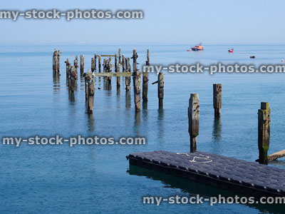 Stock image of old rotting wooden pier stacks posts, reflecting in sea