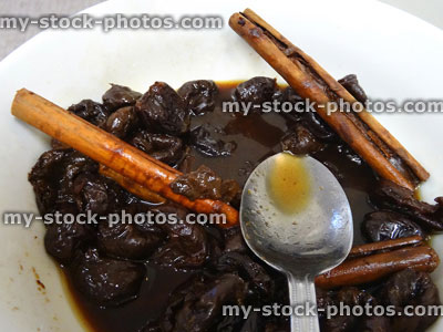 Stock image of soaked dried prunes with cinnamon sticks, healthy breakfast