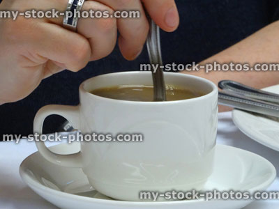 Stock image of hand stirring cup of coffee, white cup / saucer
