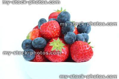 Stock image of fresh organic strawberries and blueberries, small white dish